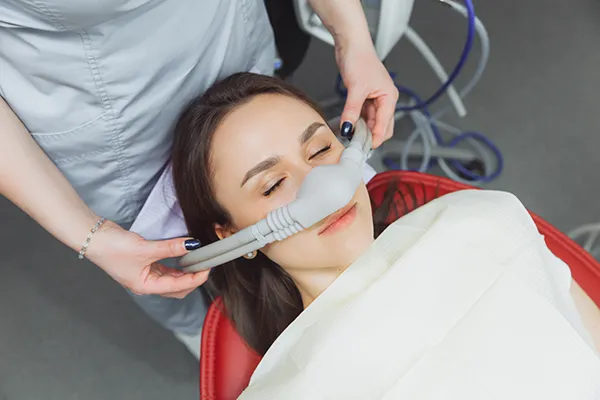 Dental assistant fitting a sedation mask over the nose of her calm female patient at Placentia Oral Surgery in Placentia, CA