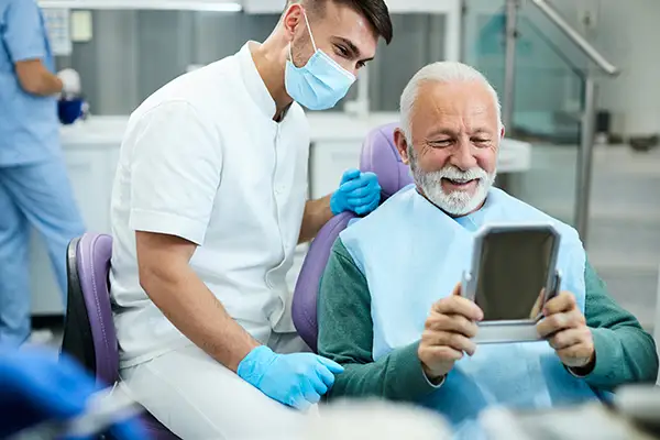 Happy, senior patient looking at himself in a mirror at Placentia Oral Surgery in Placentia, CA